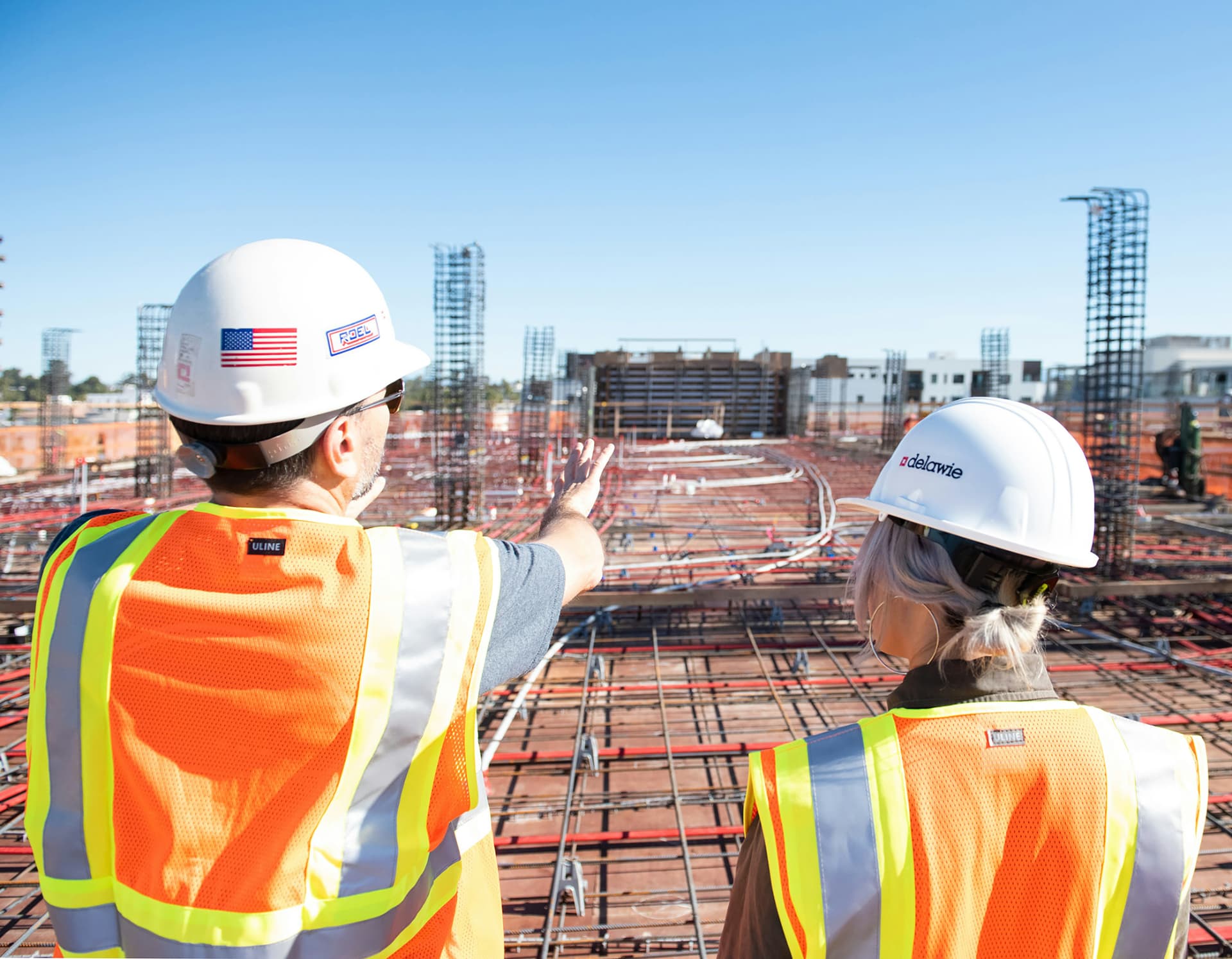 Two construction professionals in hard hats reviewing an active rebar and conduit slab pour from above