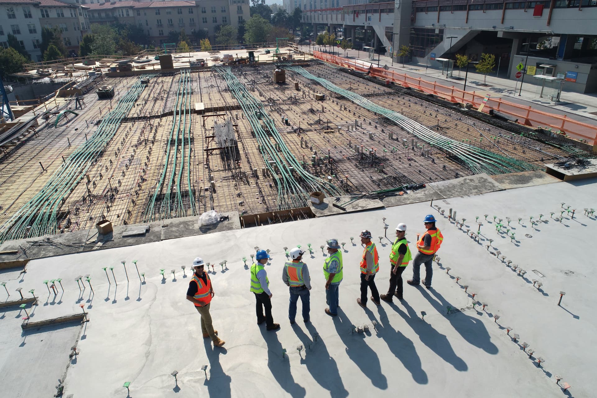 Aerial view of a construction crew standing on a large concrete deck beside a rebar mat